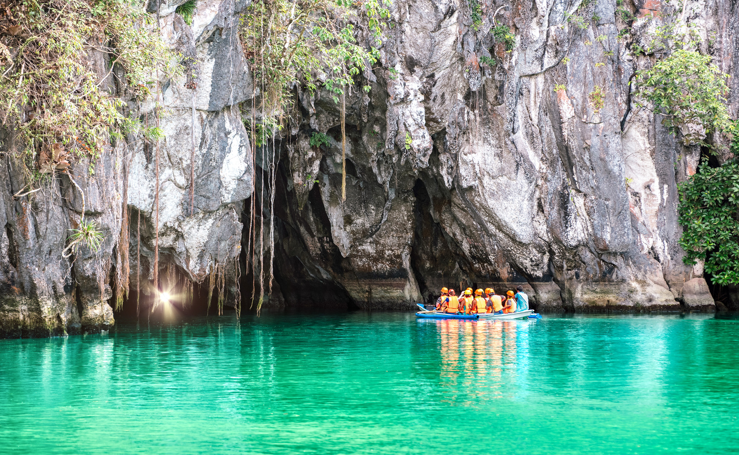 Cave entrance of Puerto Princesa subterranean underground river with longtail boat - Wanderlust travel concept at Palawan exclusive Philippine destination - Vivid filter with bulb torch light sunflare